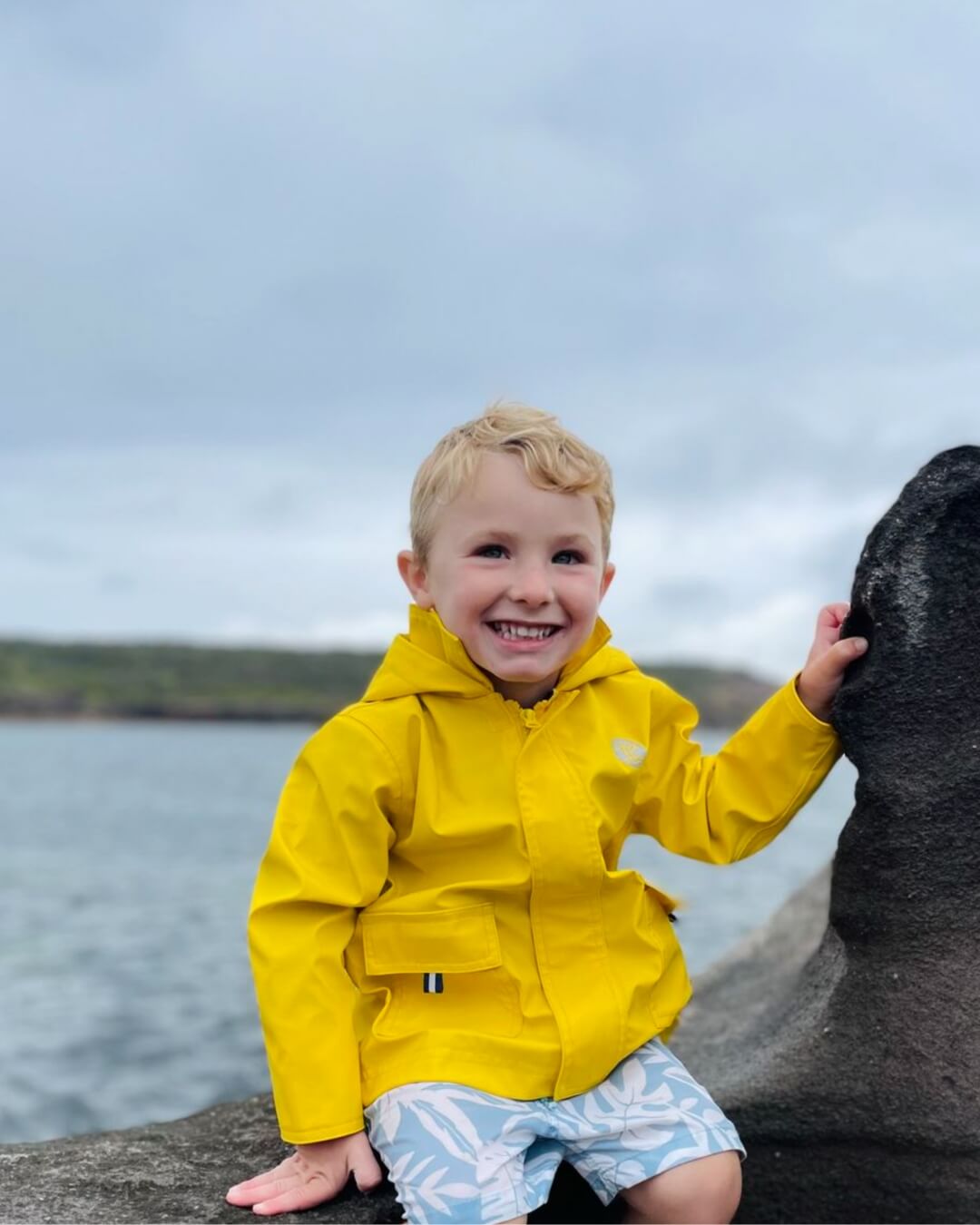 Smiling boy wearing yellow raincoat by ocean