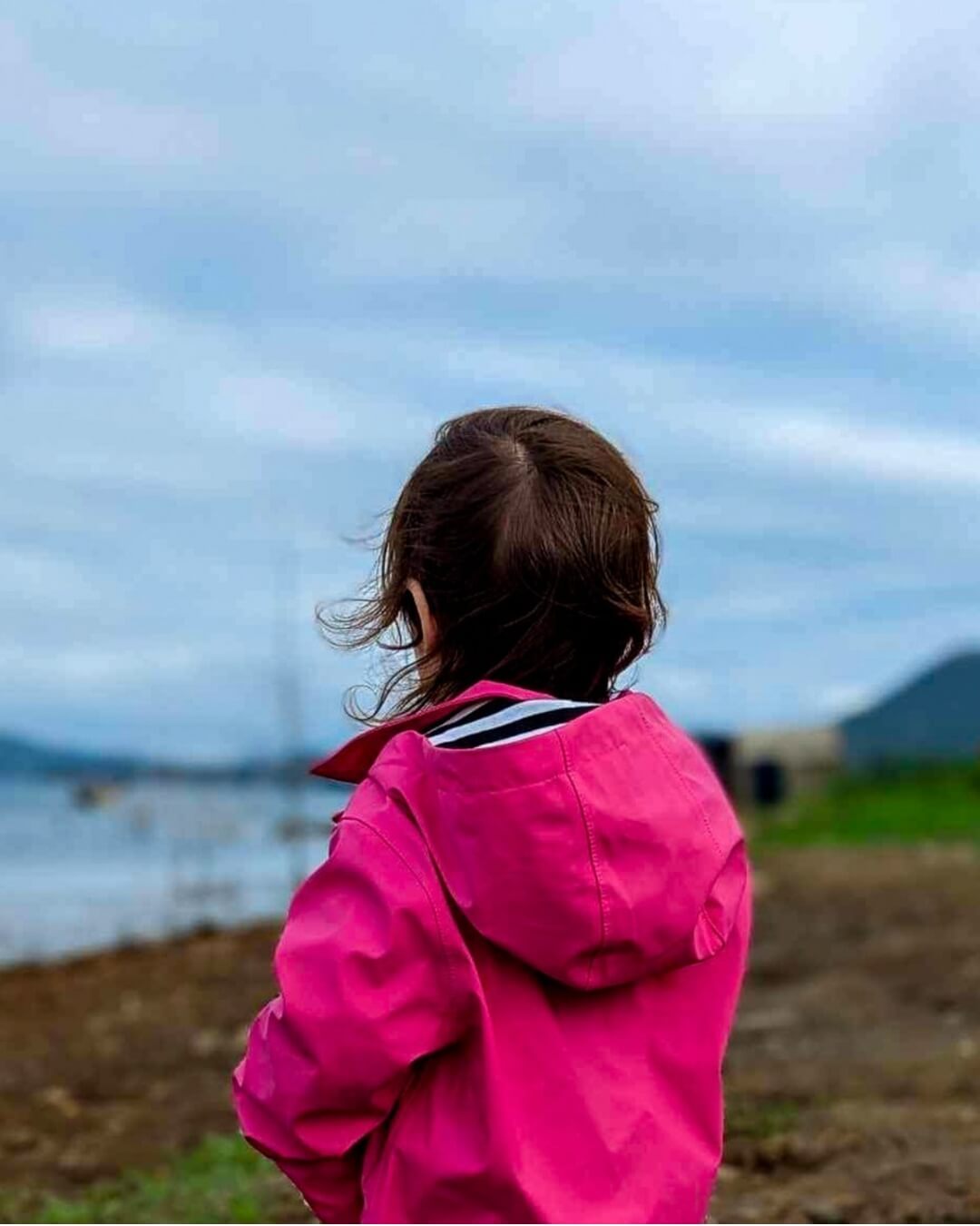girl wearing pink rain jacket looking at the lake