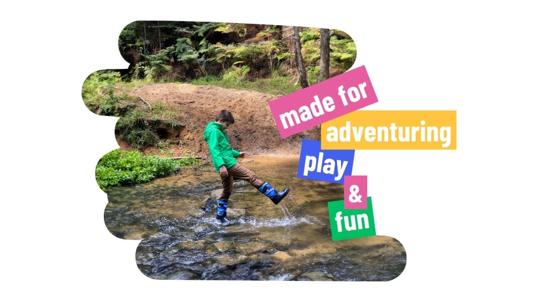 Boy wearing green raincoat and blue rain boots playing in stream