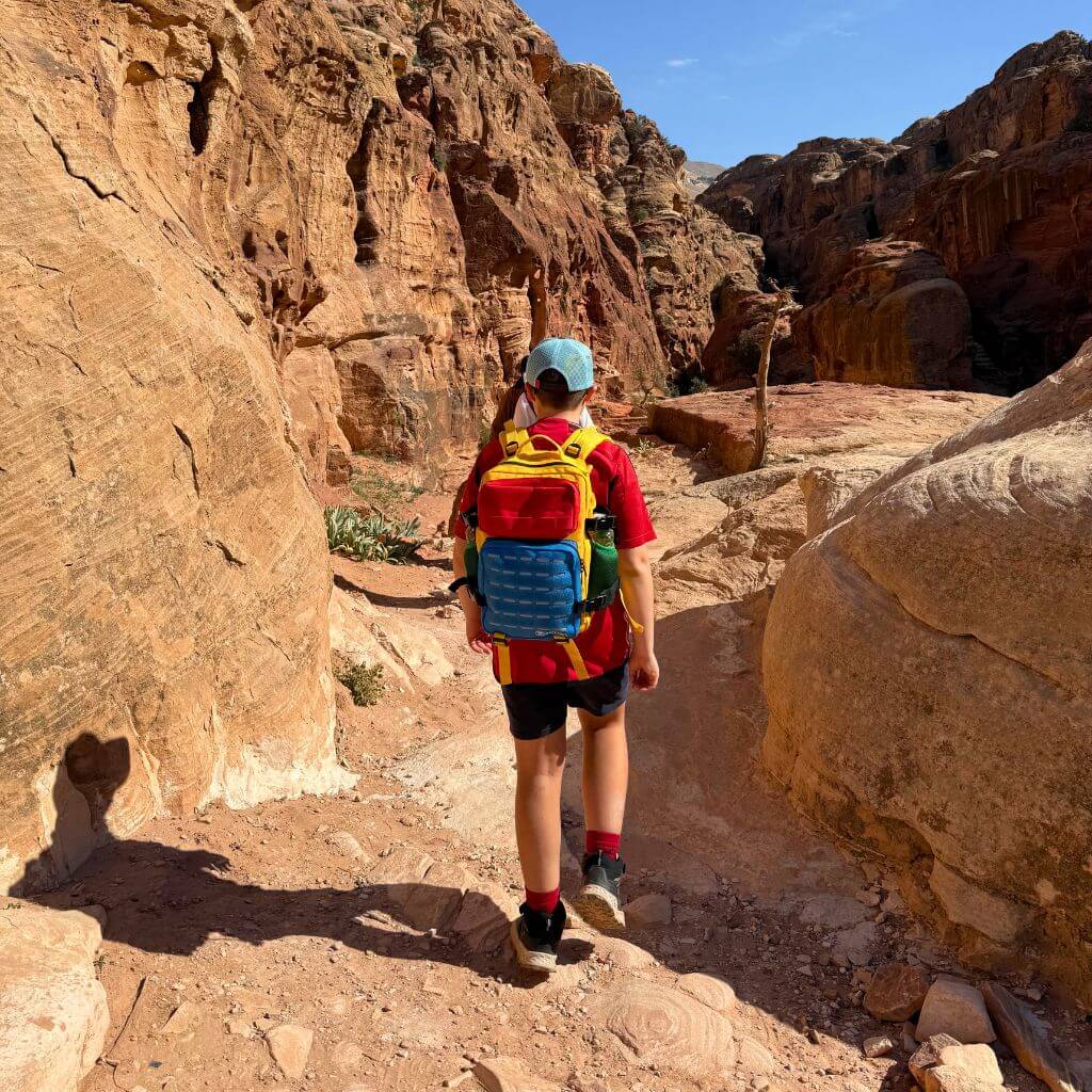 Boy hiking in desert wearing colourful backpack and cap