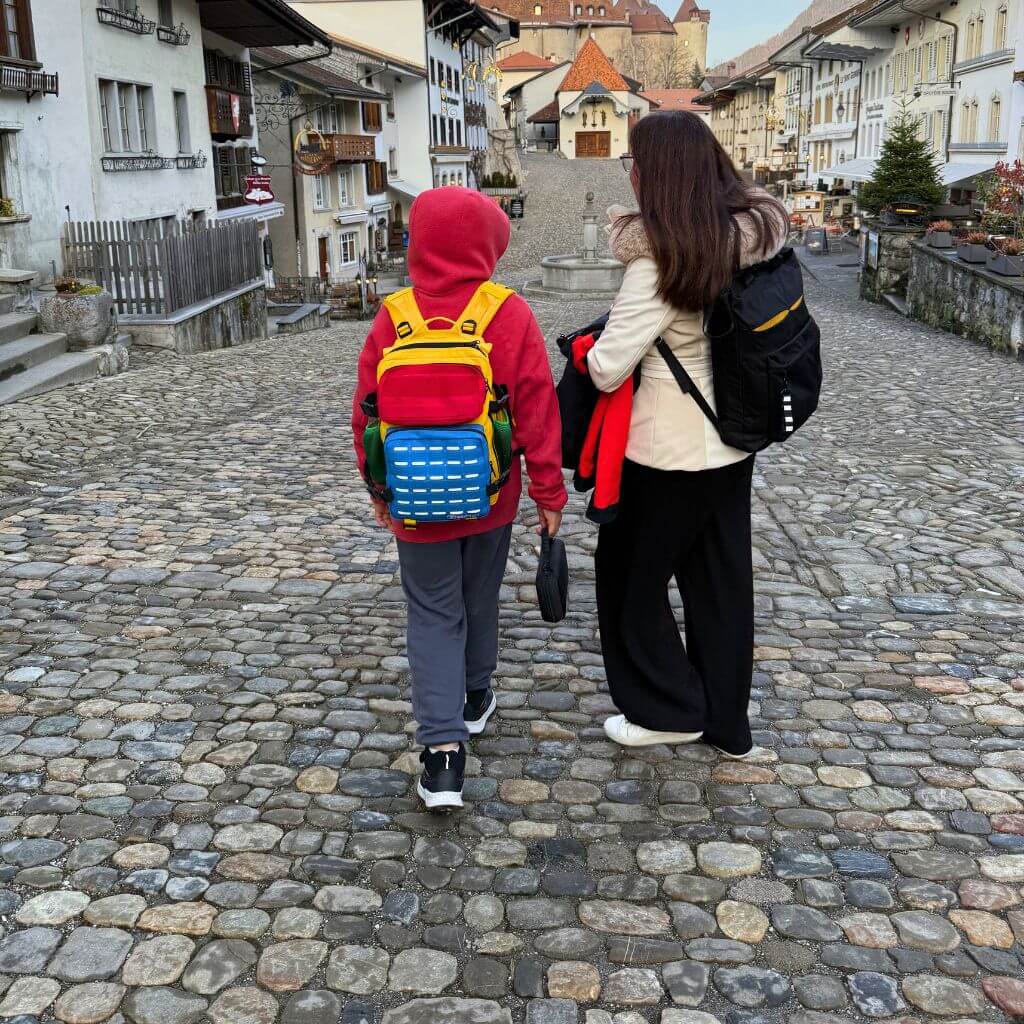 Boy wearing colourful backpack exploring Gruyere village with his mum