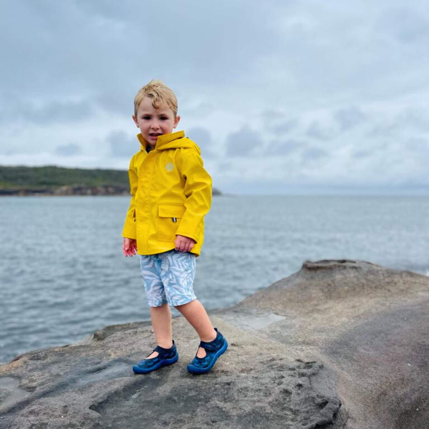 Boy wearing Yellow Seafarer Raincoat by Wavetree next to ocean