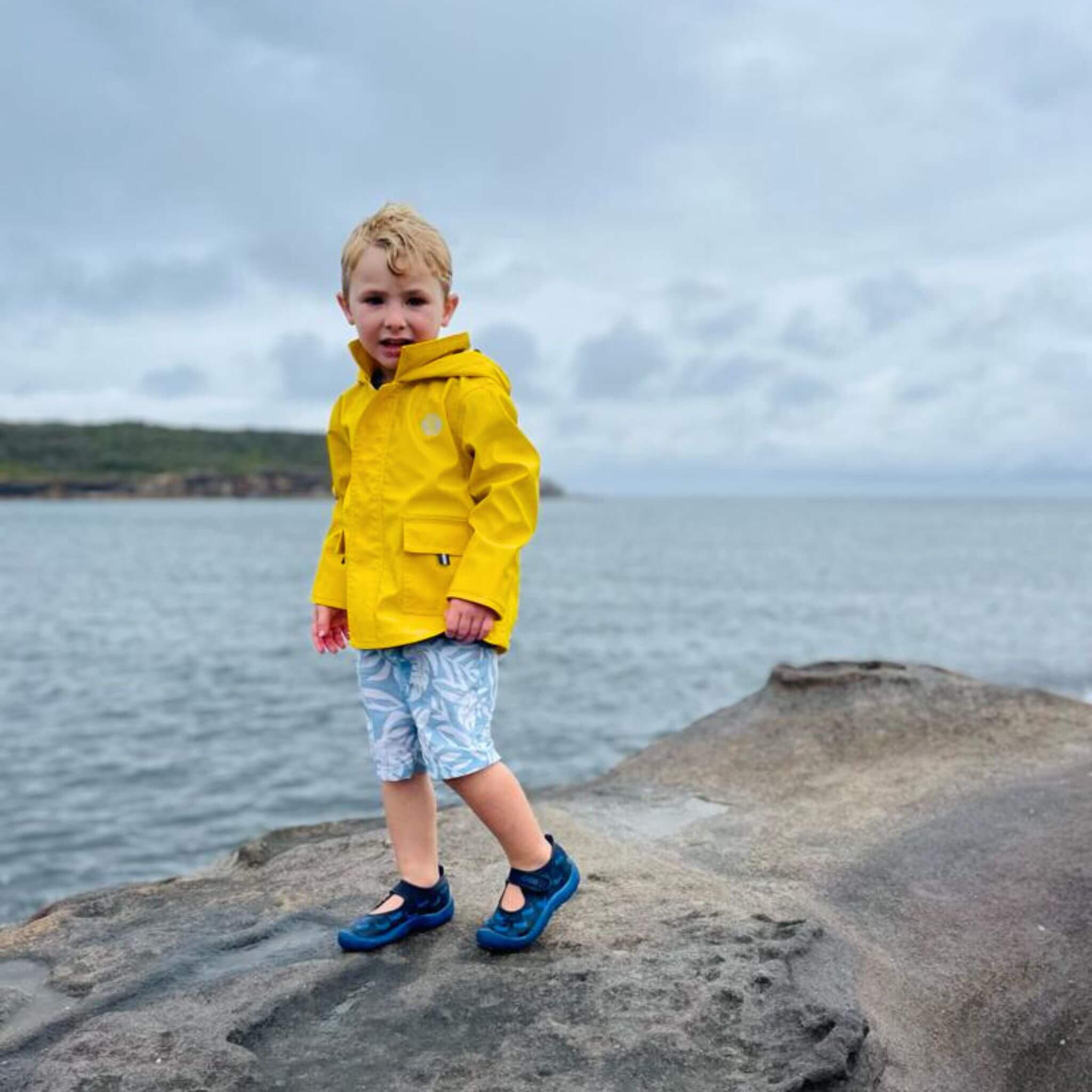 Boy wearing Yellow Seafarer Raincoat by Wavetree next to ocean