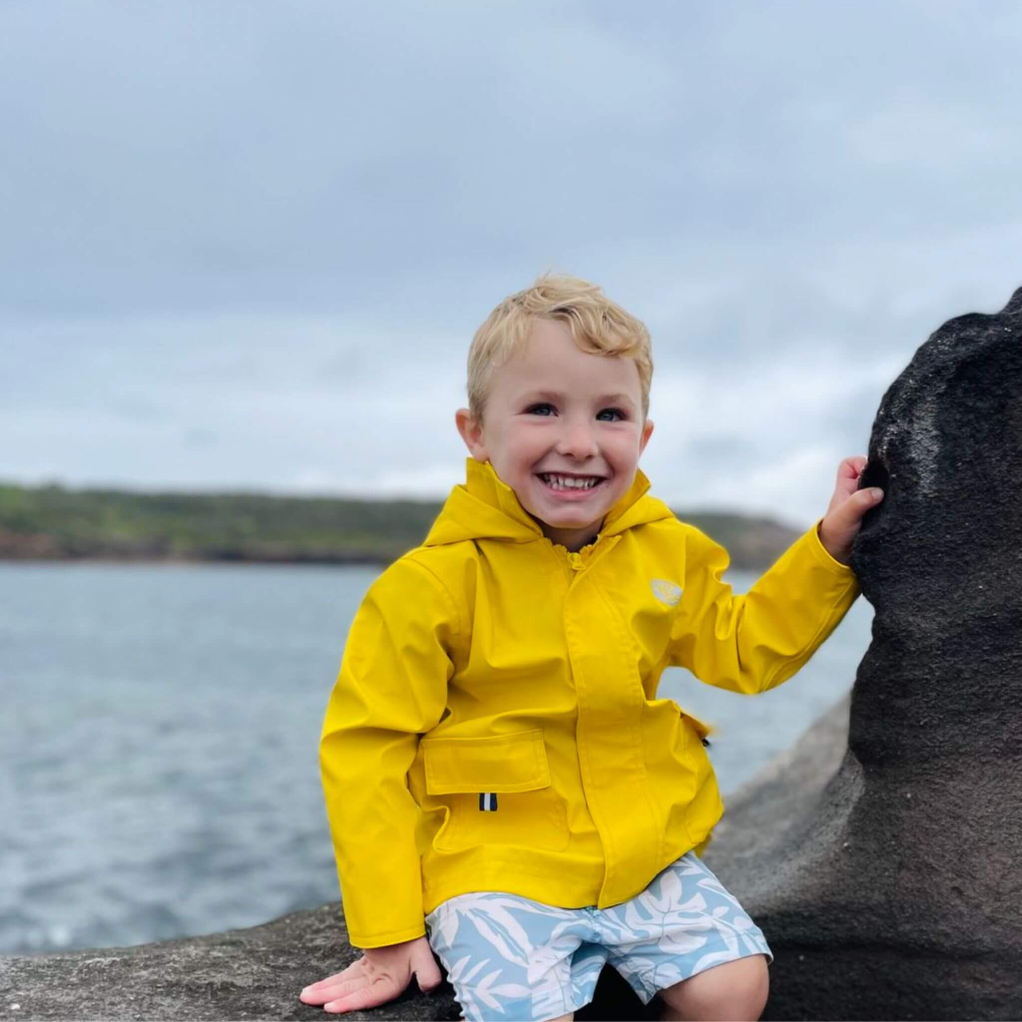Boy wearing Yellow Seafarer Raincoat by Wavetree next to ocean