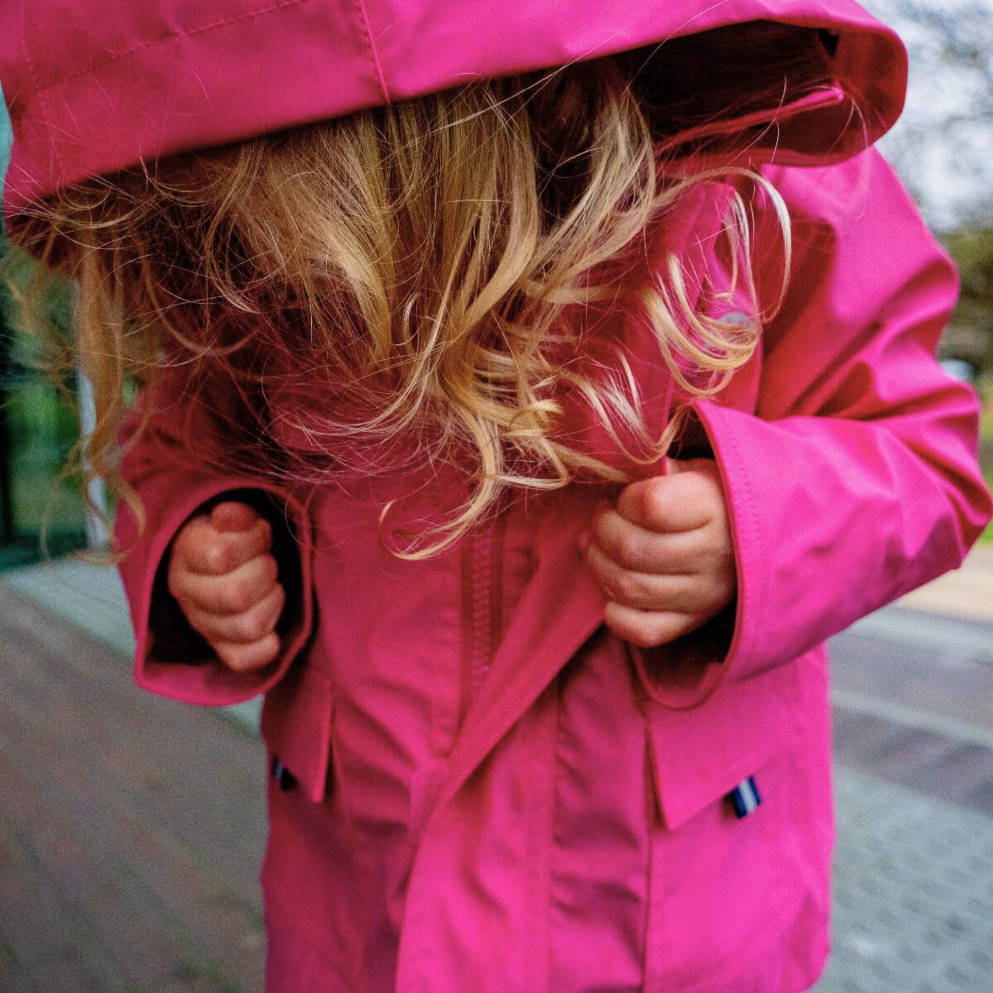 Girl with blond hair putting on pink Raincoat by Wavetree