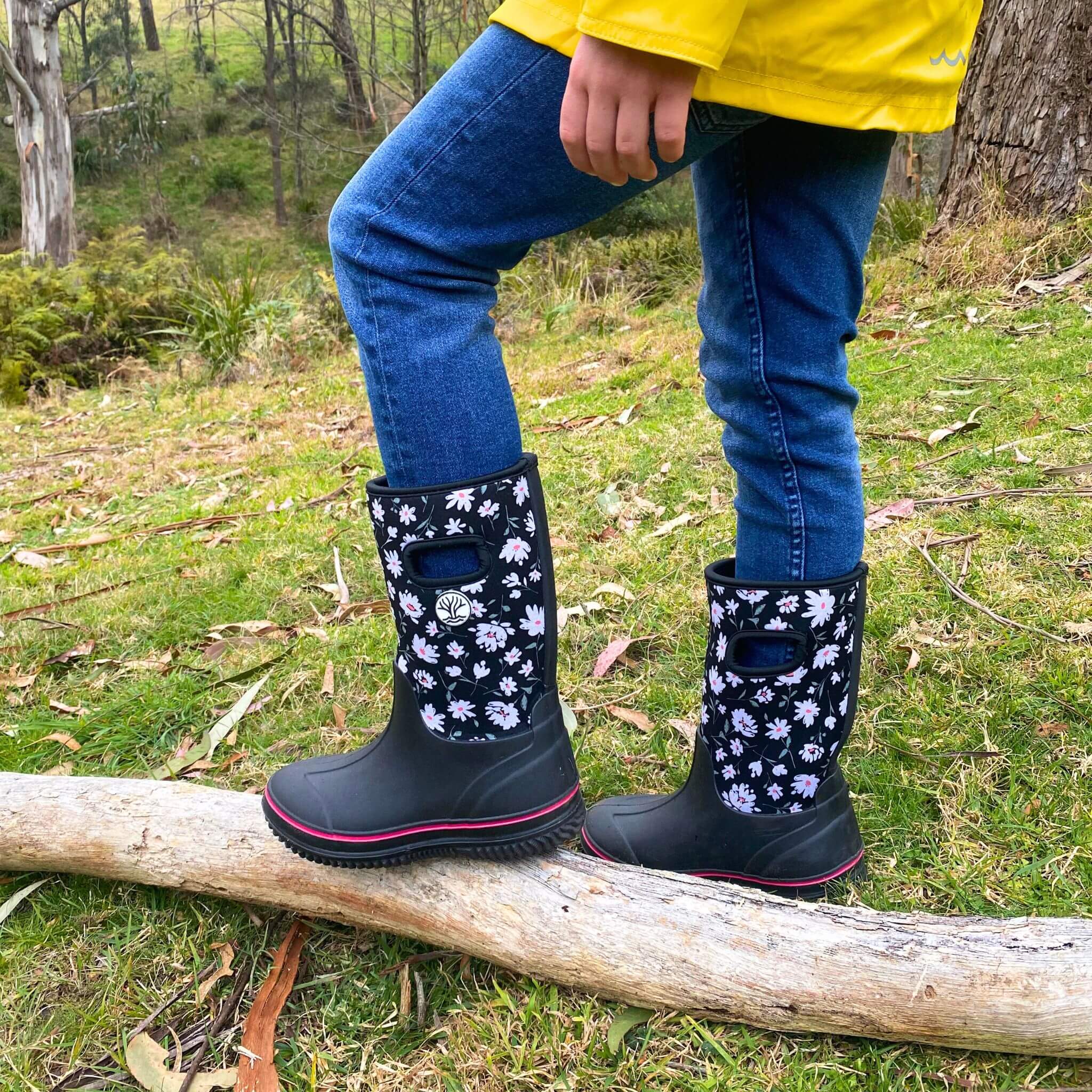 Girl with daisy pattern gumboots standing on tree branch on grass in the bush